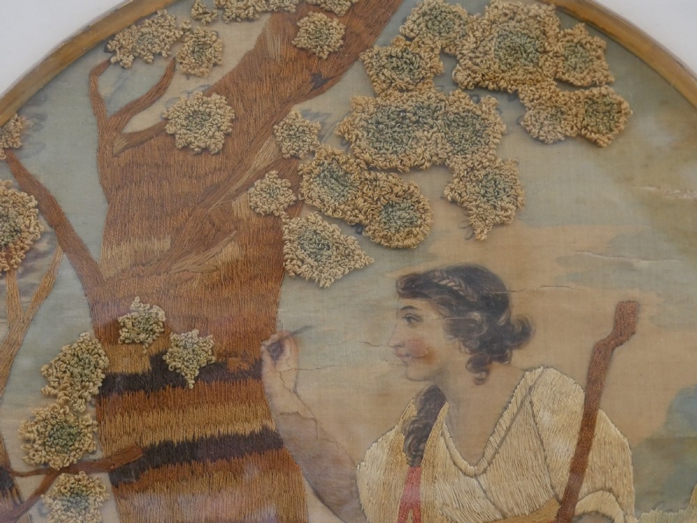 An early nineteenth-century oval crewel work embroidery depicting a shepherdess under a tree with sheep, set in a carved giltwood frame. View X