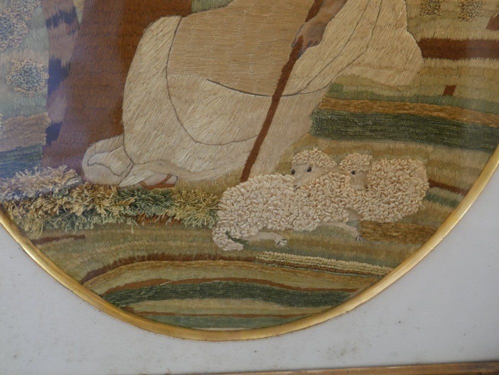 An early nineteenth-century oval crewel work embroidery depicting a shepherdess under a tree with sheep, set in a carved giltwood frame. View III