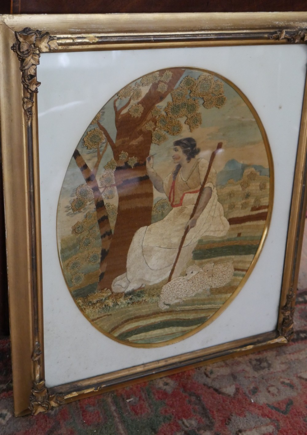 An early nineteenth-century oval crewel work embroidery depicting a shepherdess under a tree with sheep, set in a carved giltwood frame. View XIV