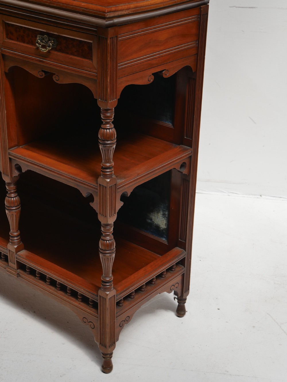 A late Victorian walnut and amboyna mirrored-back sideboard featuring carved panel doors, open tier shelving, turned spindles, and top finials. View II