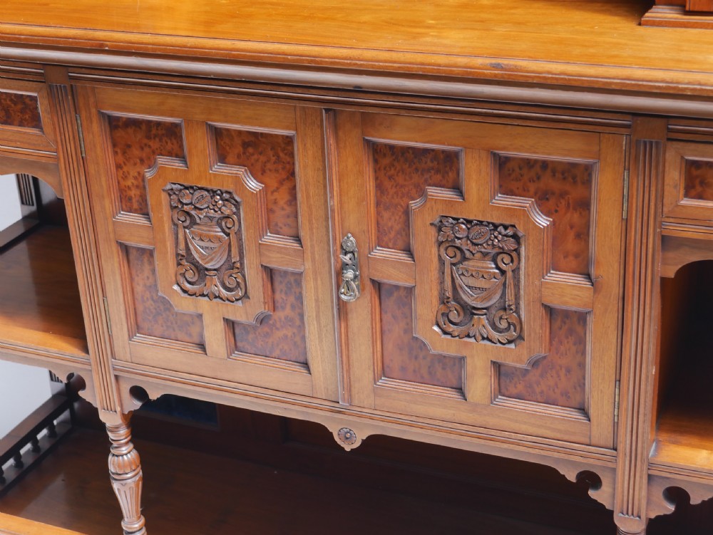 A late Victorian walnut and amboyna mirrored-back sideboard featuring carved panel doors, open tier shelving, turned spindles, and top finials. View III