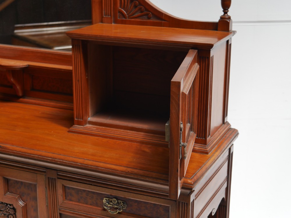 A late Victorian walnut and amboyna mirrored-back sideboard featuring carved panel doors, open tier shelving, turned spindles, and top finials. View VII