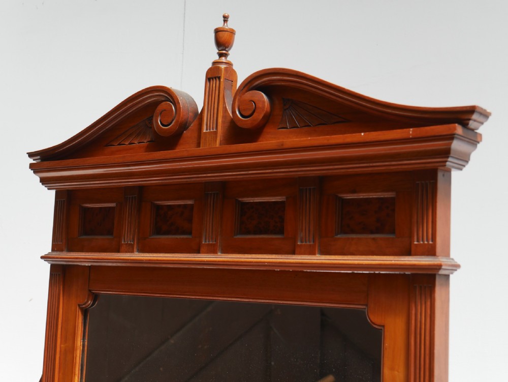 A late Victorian walnut and amboyna mirrored-back sideboard featuring carved panel doors, open tier shelving, turned spindles, and top finials. View X