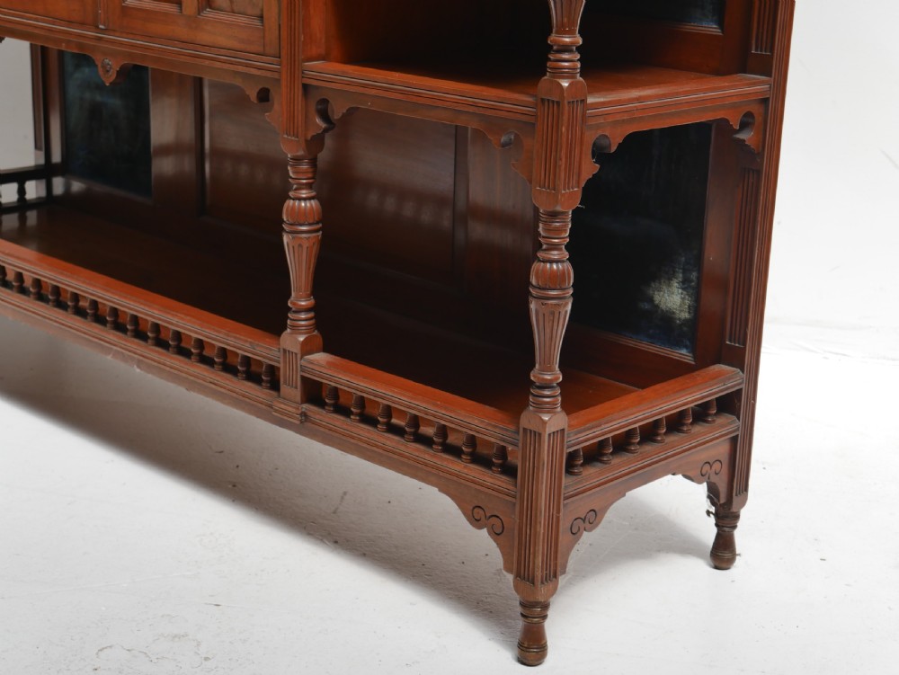 A late Victorian walnut and amboyna mirrored-back sideboard featuring carved panel doors, open tier shelving, turned spindles, and top finials. View XI