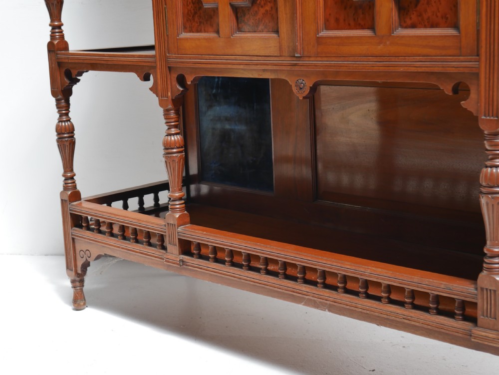A late Victorian walnut and amboyna mirrored-back sideboard featuring carved panel doors, open tier shelving, turned spindles, and top finials. View XII