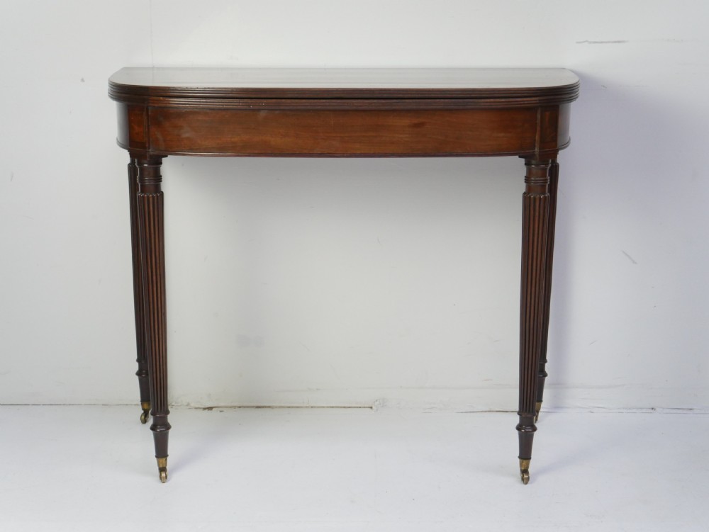 A Regency mahogany fold-over table featuring a demilune top, reeded legs, and brass castors.