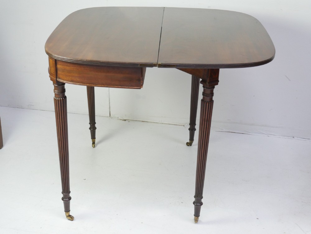 A Regency mahogany fold-over table featuring a demilune top, reeded legs, and brass castors. View VII