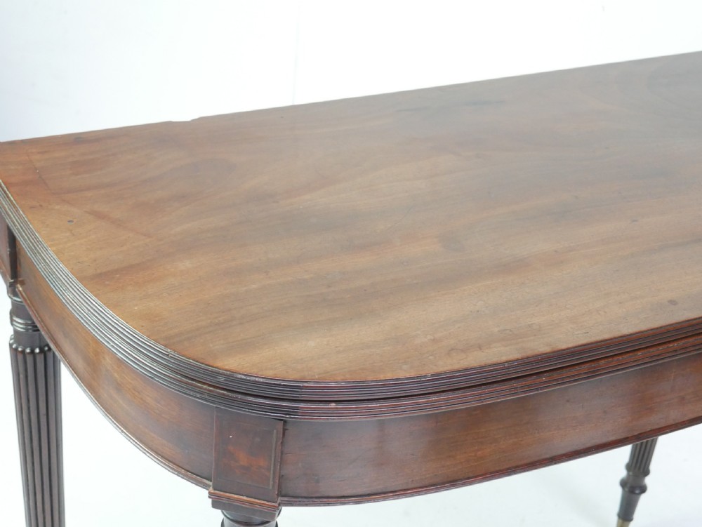 A Regency mahogany fold-over table featuring a demilune top, reeded legs, and brass castors. View VIII