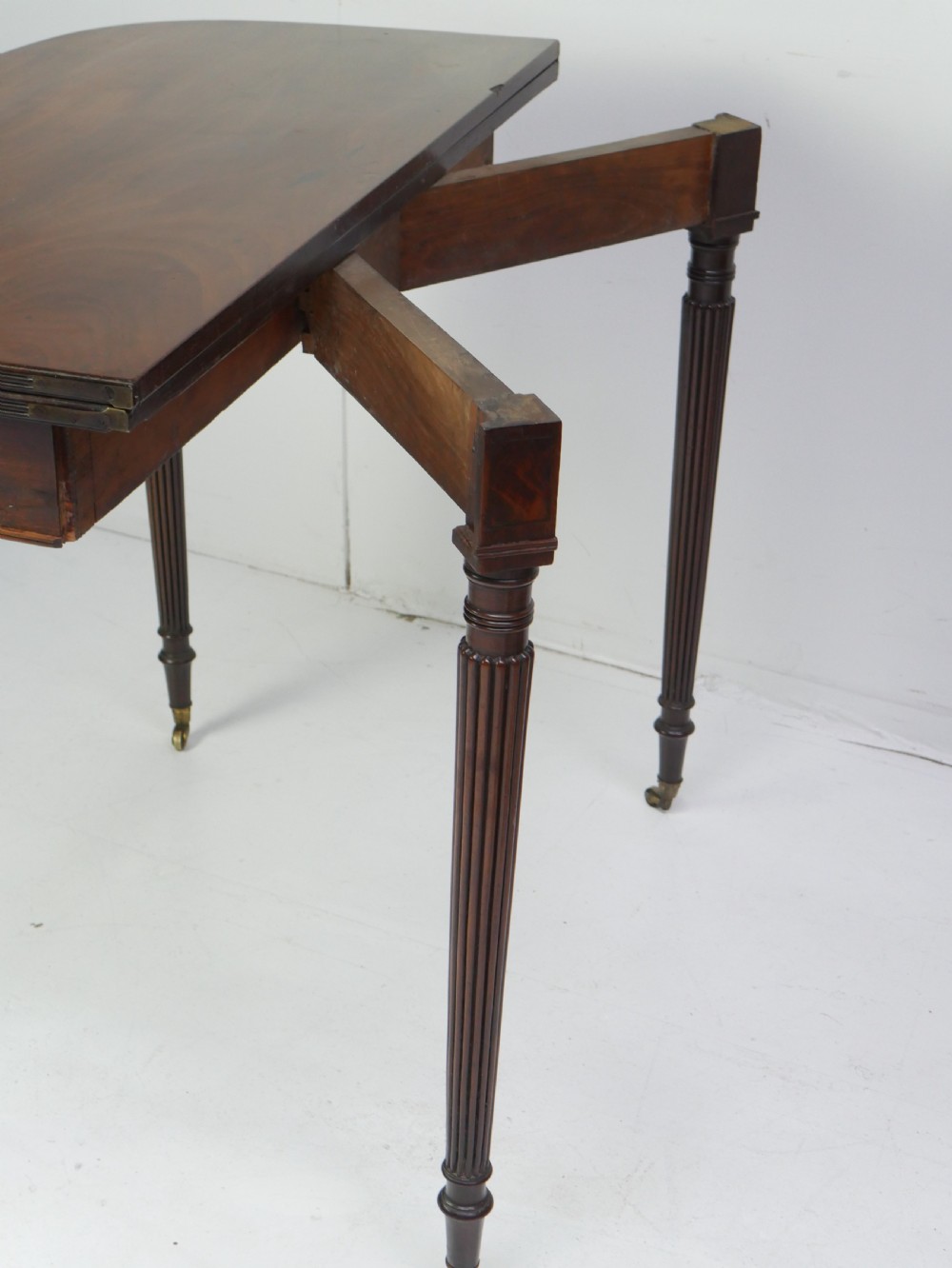 A Regency mahogany fold-over table featuring a demilune top, reeded legs, and brass castors. View IX
