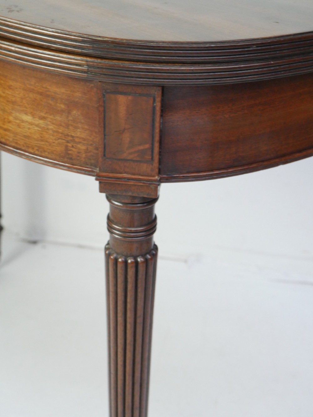 A Regency mahogany fold-over table featuring a demilune top, reeded legs, and brass castors. View XII