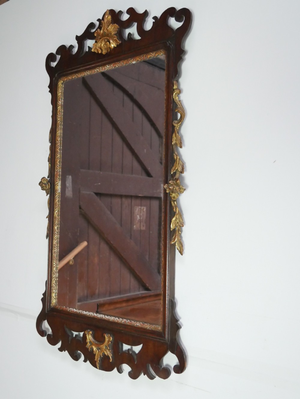 A rectangular Georgian mahogany wall mirror featuring a scroll-cut fretwork frame ornamented with giltwood leaves and cresting.