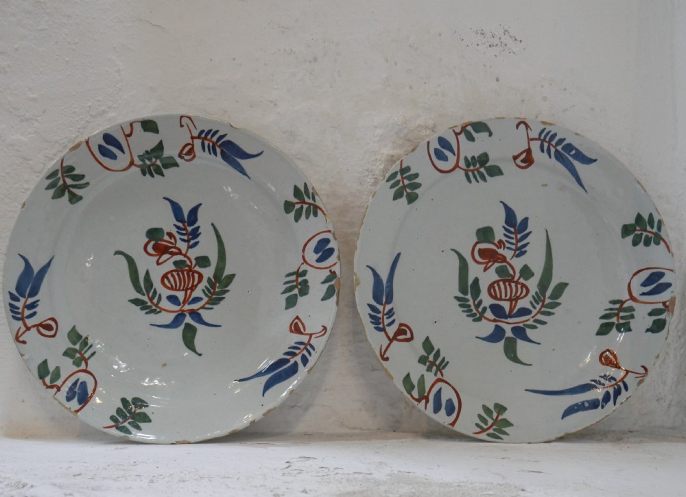 A pair of circular tin-glazed earthenware plates with off-white glaze, decorated with hand-painted polychrome floral motifs in blue, green, and iron-red.