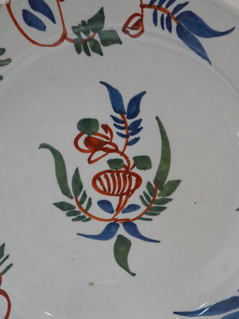 A pair of circular tin-glazed earthenware plates with off-white glaze, decorated with hand-painted polychrome floral motifs in blue, green, and iron-red. View II