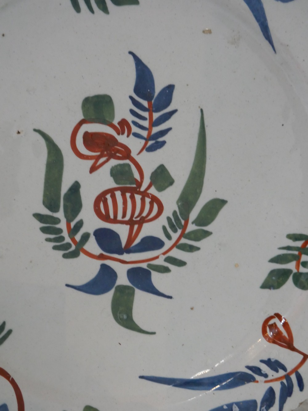 A pair of circular tin-glazed earthenware plates with off-white glaze, decorated with hand-painted polychrome floral motifs in blue, green, and iron-red. View III