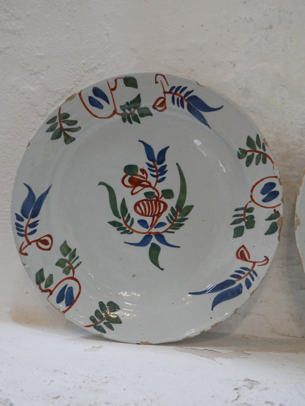 A pair of circular tin-glazed earthenware plates with off-white glaze, decorated with hand-painted polychrome floral motifs in blue, green, and iron-red. View V