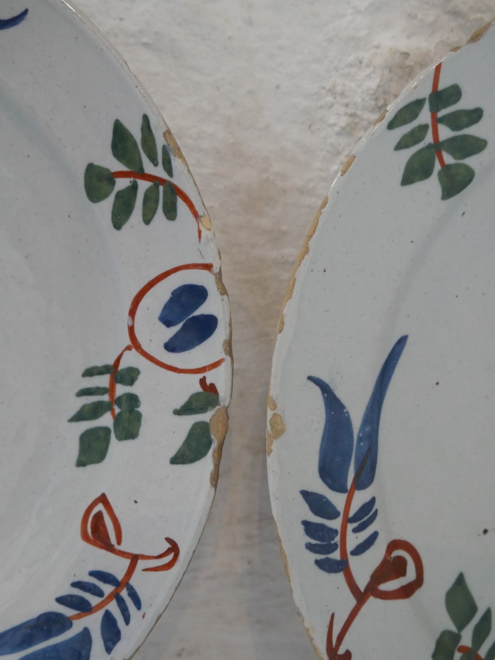 A pair of circular tin-glazed earthenware plates with off-white glaze, decorated with hand-painted polychrome floral motifs in blue, green, and iron-red. View VII