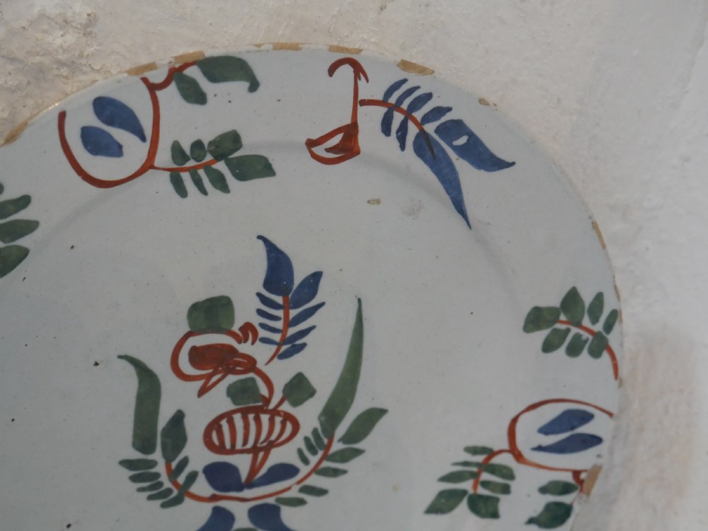 A pair of circular tin-glazed earthenware plates with off-white glaze, decorated with hand-painted polychrome floral motifs in blue, green, and iron-red. View VIII