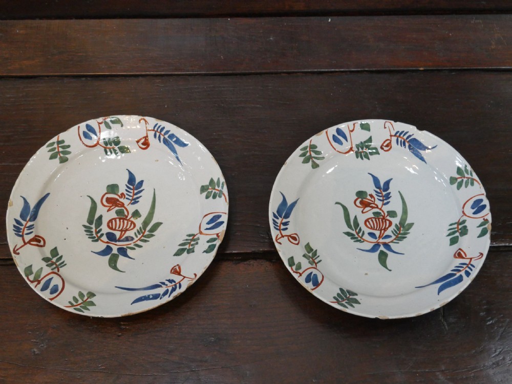 A pair of circular tin-glazed earthenware plates with off-white glaze, decorated with hand-painted polychrome floral motifs in blue, green, and iron-red. View IX