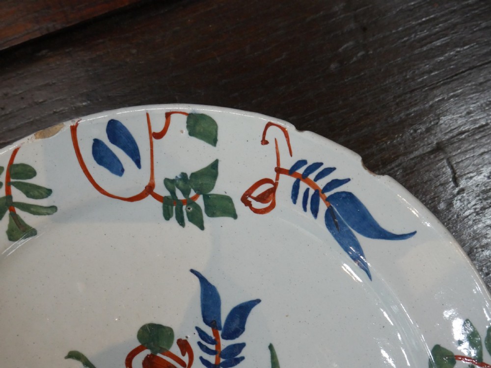 A pair of circular tin-glazed earthenware plates with off-white glaze, decorated with hand-painted polychrome floral motifs in blue, green, and iron-red. View XIV