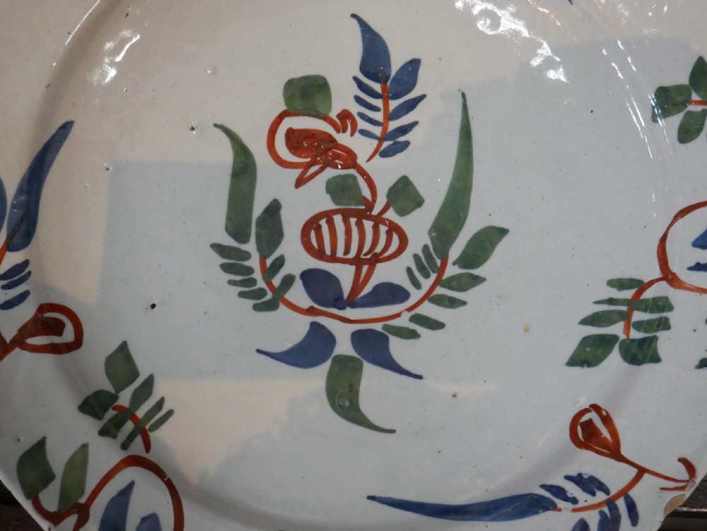 A pair of circular tin-glazed earthenware plates with off-white glaze, decorated with hand-painted polychrome floral motifs in blue, green, and iron-red. View XV