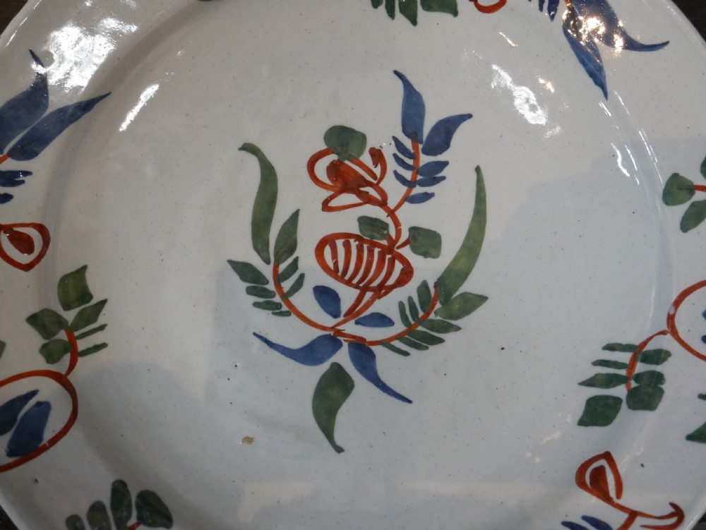 A pair of circular tin-glazed earthenware plates with off-white glaze, decorated with hand-painted polychrome floral motifs in blue, green, and iron-red. View XVI