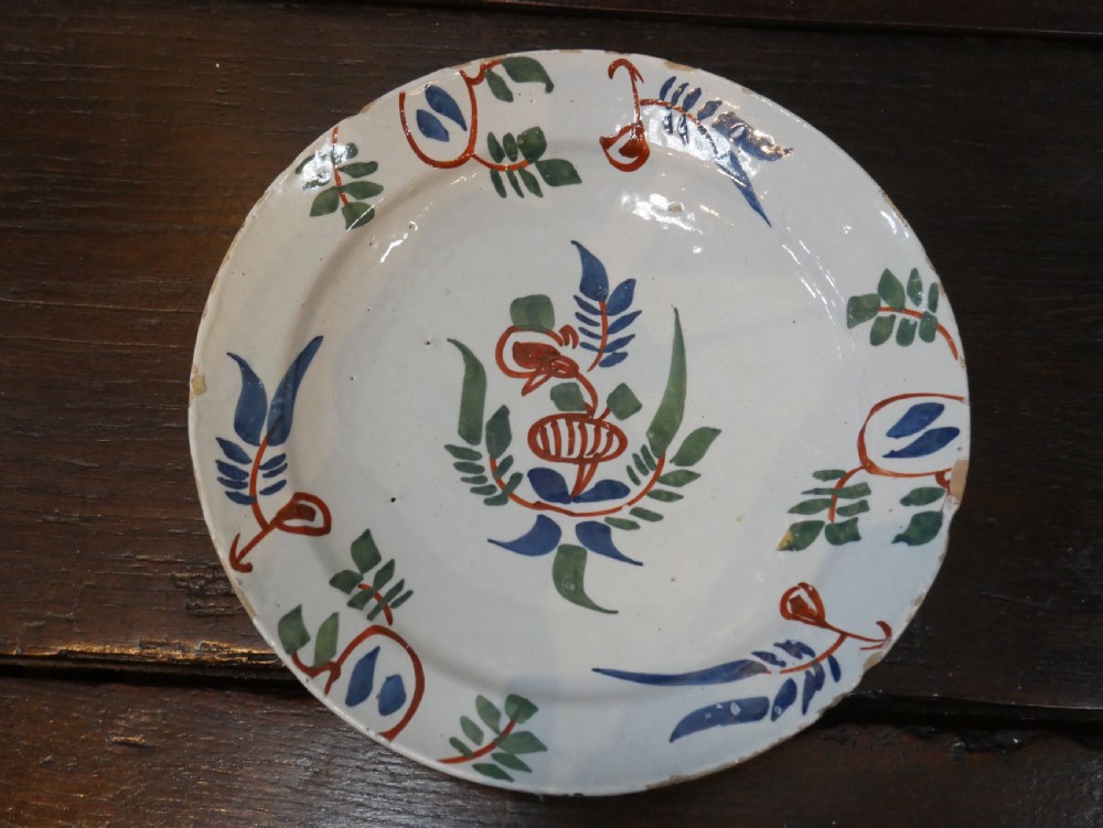 A pair of circular tin-glazed earthenware plates with off-white glaze, decorated with hand-painted polychrome floral motifs in blue, green, and iron-red. View XVII