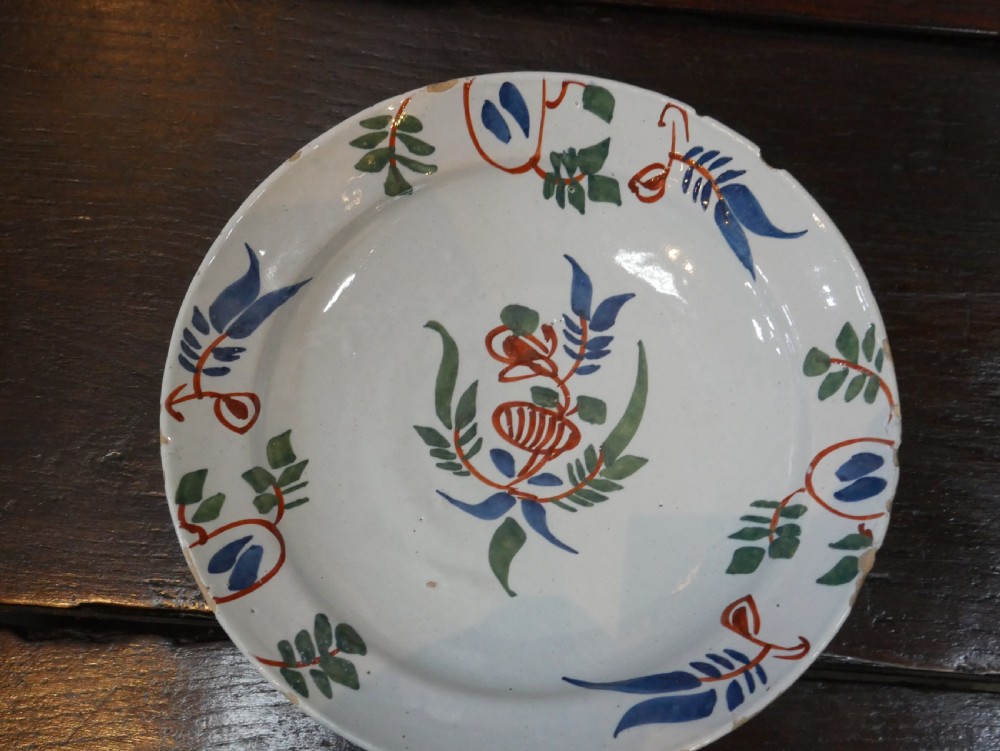 A pair of circular tin-glazed earthenware plates with off-white glaze, decorated with hand-painted polychrome floral motifs in blue, green, and iron-red. View XVIII
