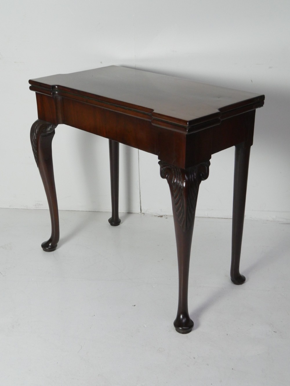 A Georgian mahogany fold-over games table featuring carved cabriole front legs with pad feet and a rectangular top with turret corners.