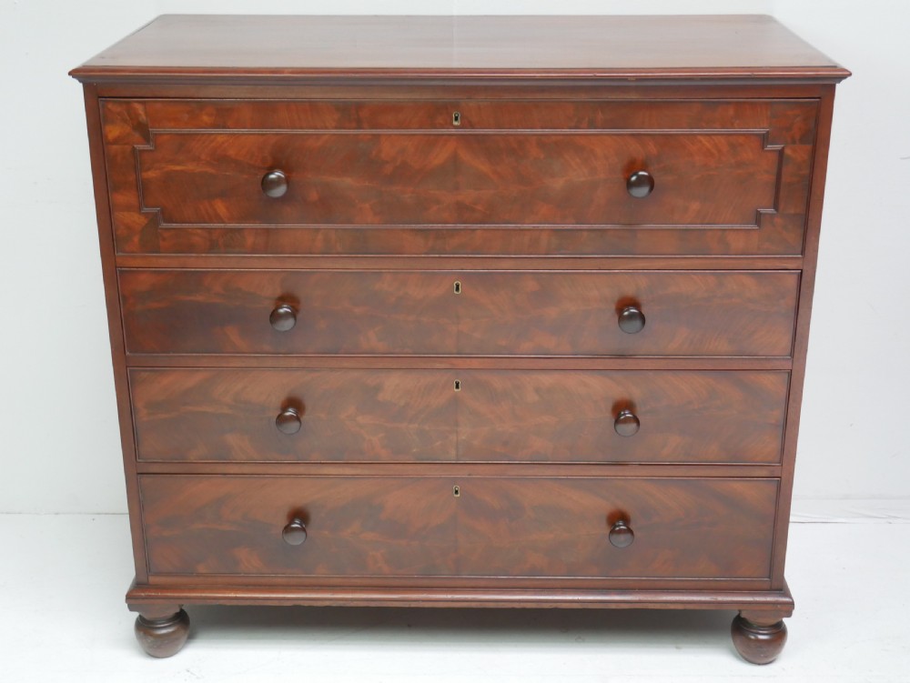A classic Regency mahogany chest featuring four horizontal drawers with flame mahogany grain, turned wooden knobs, brass keyhole escutcheons, and turned feet.