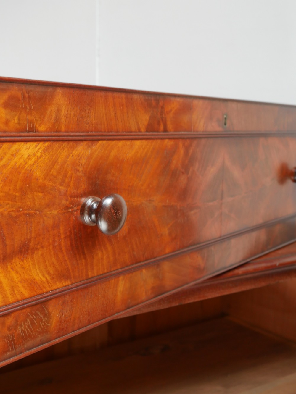 A classic Regency mahogany chest featuring four horizontal drawers with flame mahogany grain, turned wooden knobs, brass keyhole escutcheons, and turned feet. View V