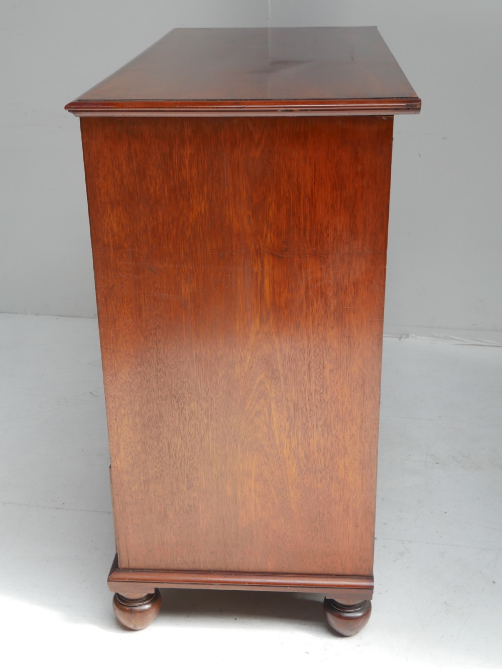 A classic Regency mahogany chest featuring four horizontal drawers with flame mahogany grain, turned wooden knobs, brass keyhole escutcheons, and turned feet. View VII