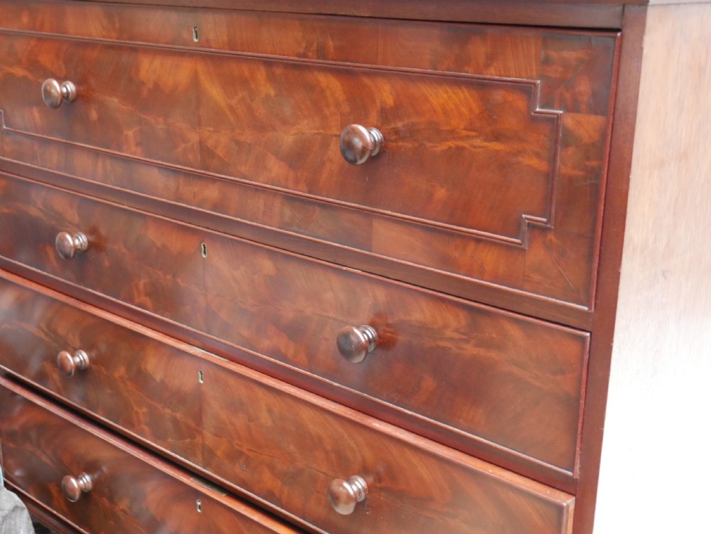 A classic Regency mahogany chest featuring four horizontal drawers with flame mahogany grain, turned wooden knobs, brass keyhole escutcheons, and turned feet. View XII