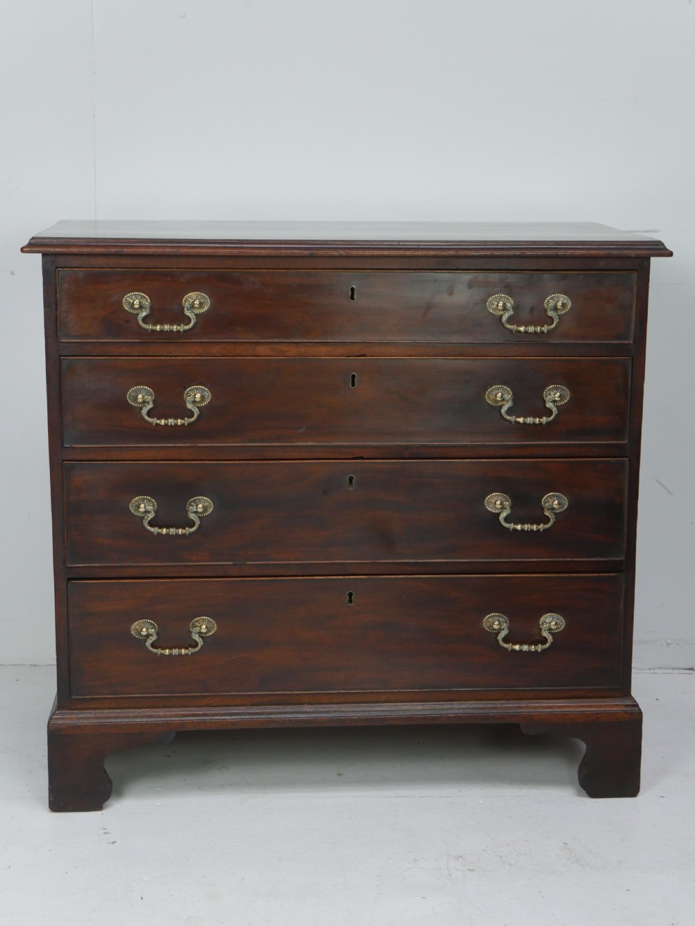 A Georgian mahogany chest of drawers featuring four graduated drawers with brass swan-neck handles and bracket feet.