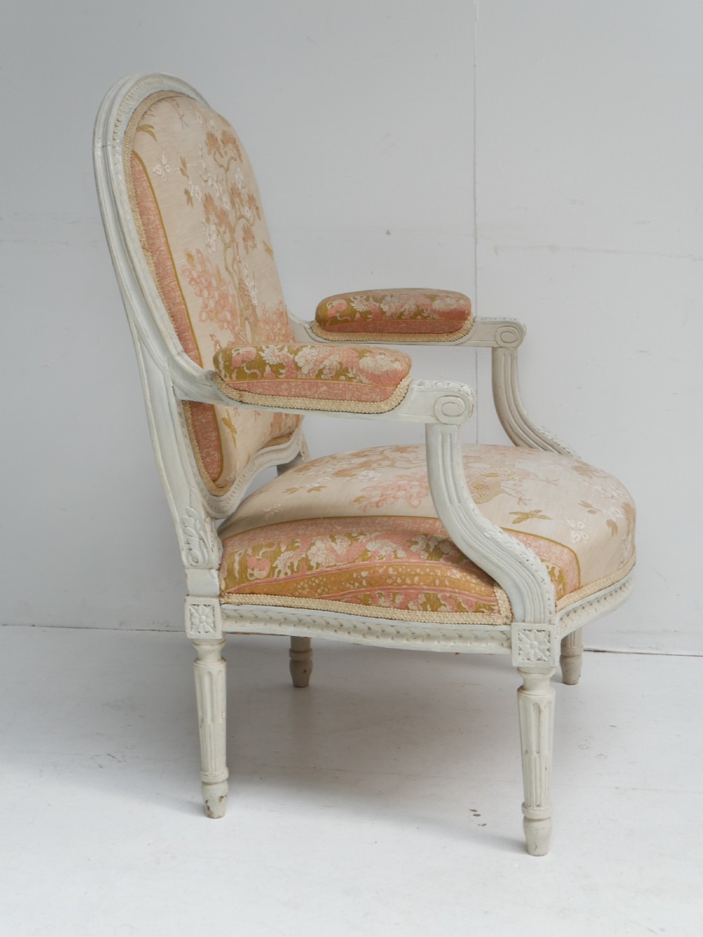 A pair of French Louis XVI style fauteuil armchairs featuring off-white painted frames, fluted legs, and patterned floral upholstery. View VIII