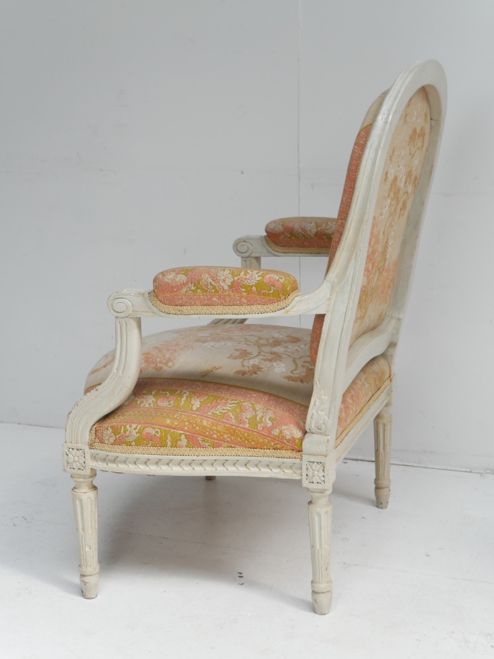 A pair of French Louis XVI style fauteuil armchairs featuring off-white painted frames, fluted legs, and patterned floral upholstery. View X