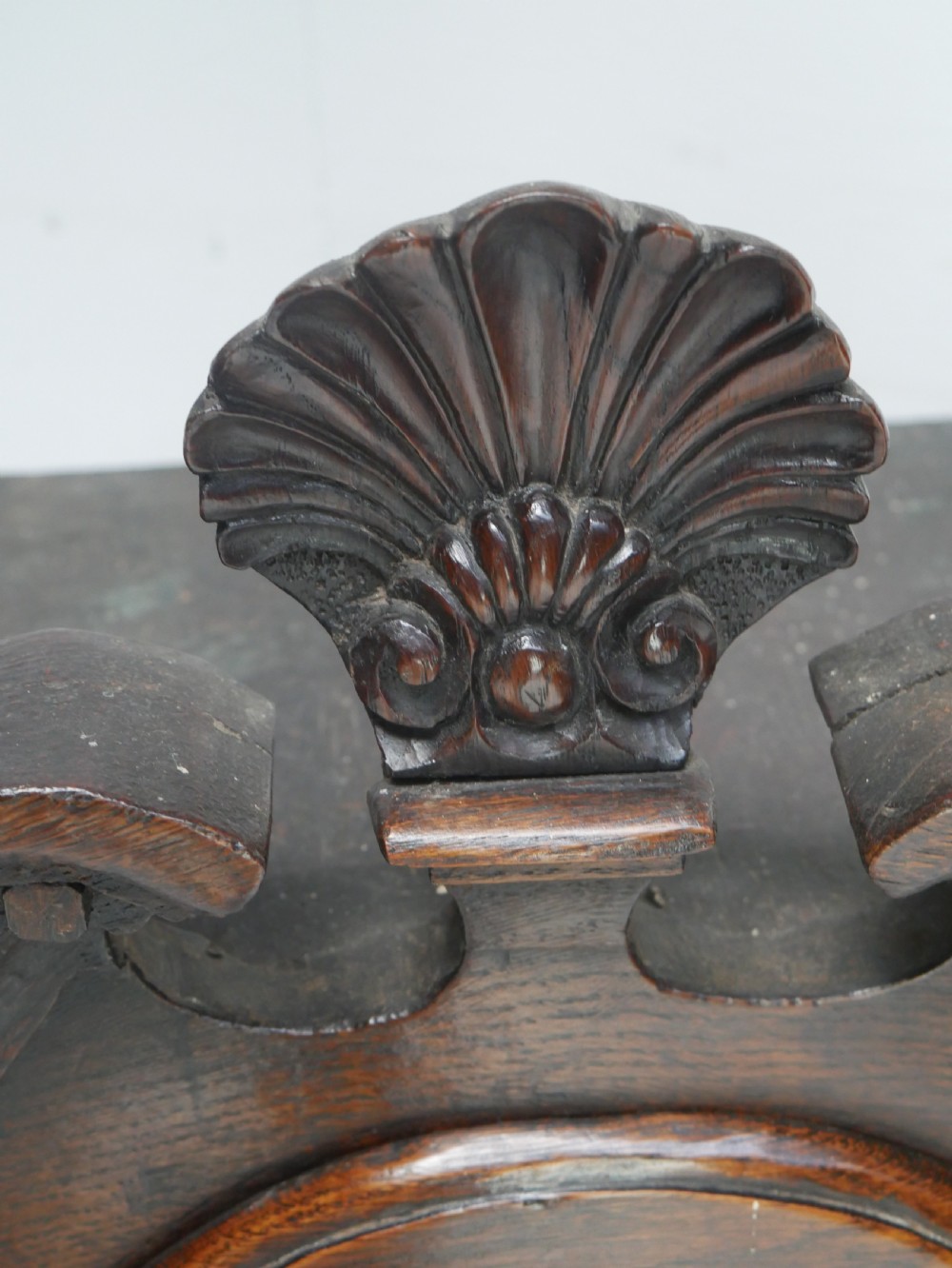 An 18th-century dark oak hanging cupboard featuring a carved shell cresting, a single fielded panel door with brass key escutcheon, and two small base drawers. View VI