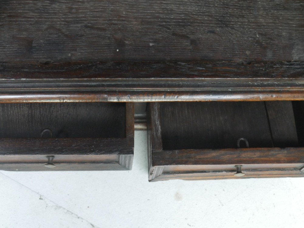 An 18th-century dark oak hanging cupboard featuring a carved shell cresting, a single fielded panel door with brass key escutcheon, and two small base drawers. View IX