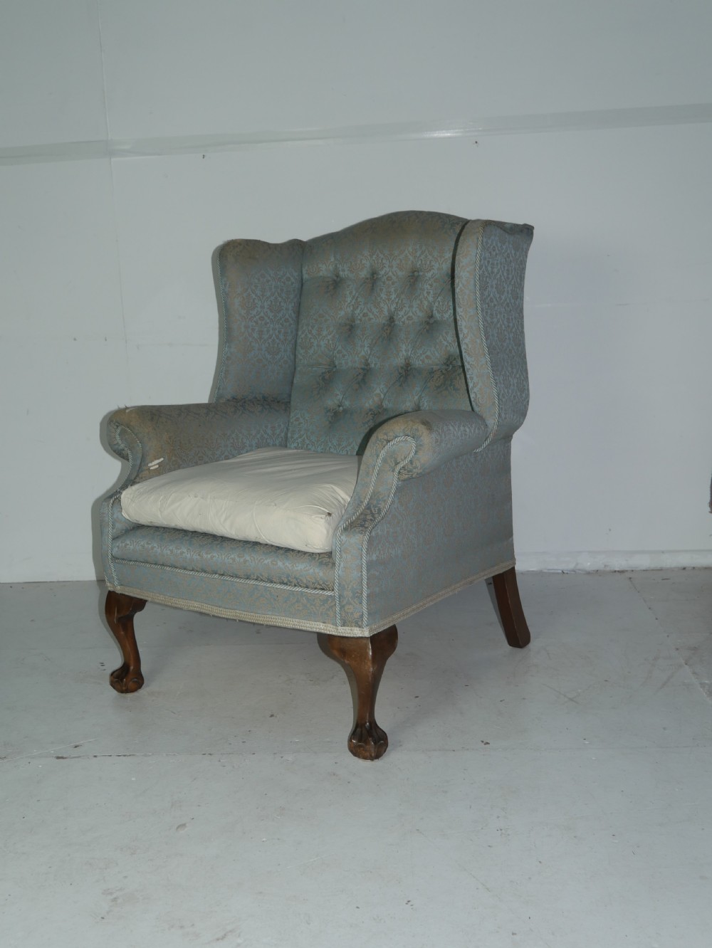 A high-backed wing armchair upholstered in patterned blue damask fabric with a deep buttoned backrest and carved wood cabriole front legs.