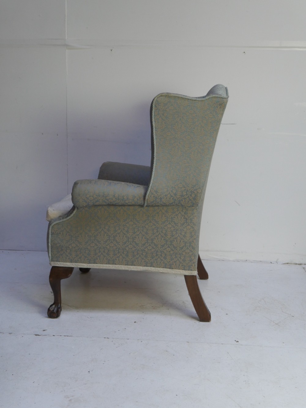 A high-backed wing armchair upholstered in patterned blue damask fabric with a deep buttoned backrest and carved wood cabriole front legs. View V