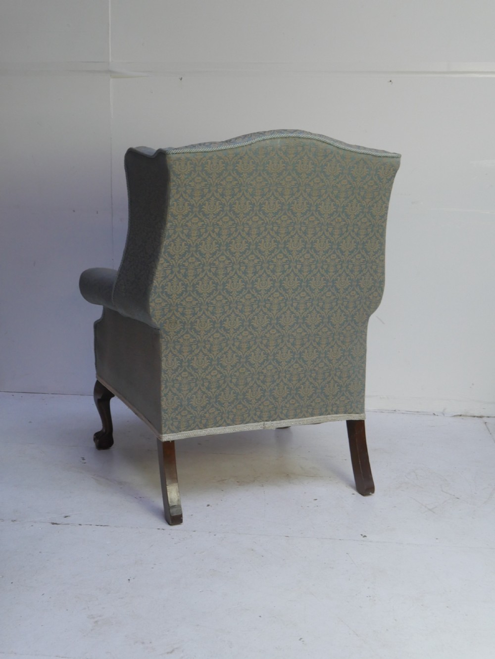 A high-backed wing armchair upholstered in patterned blue damask fabric with a deep buttoned backrest and carved wood cabriole front legs. View VI