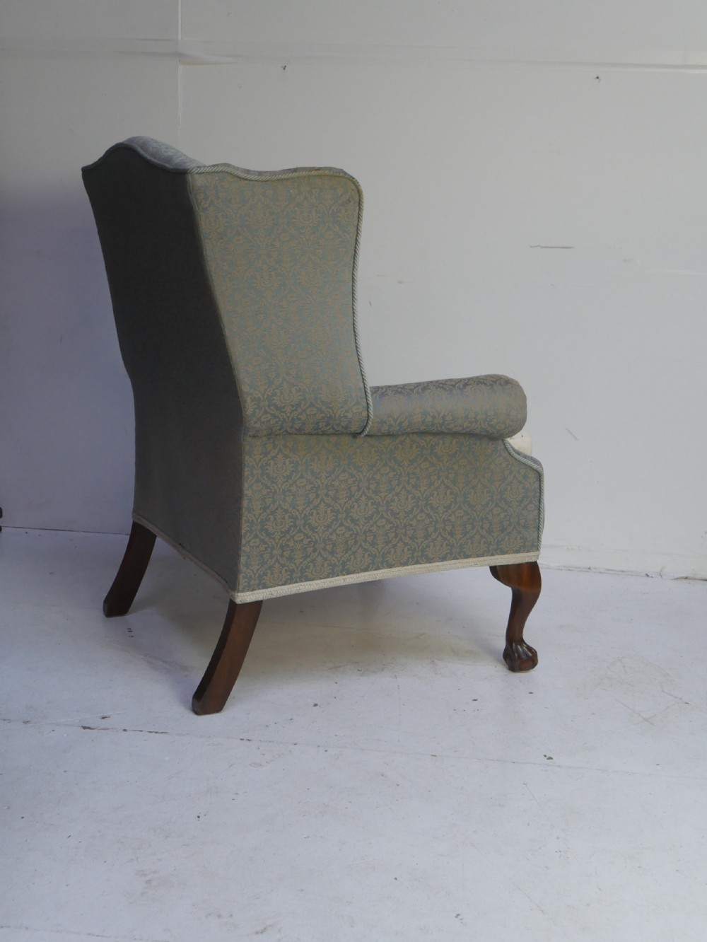 A high-backed wing armchair upholstered in patterned blue damask fabric with a deep buttoned backrest and carved wood cabriole front legs. View VII