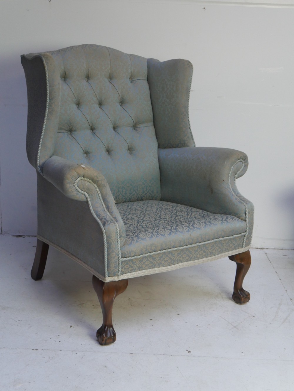 A high-backed wing armchair upholstered in patterned blue damask fabric with a deep buttoned backrest and carved wood cabriole front legs. View X