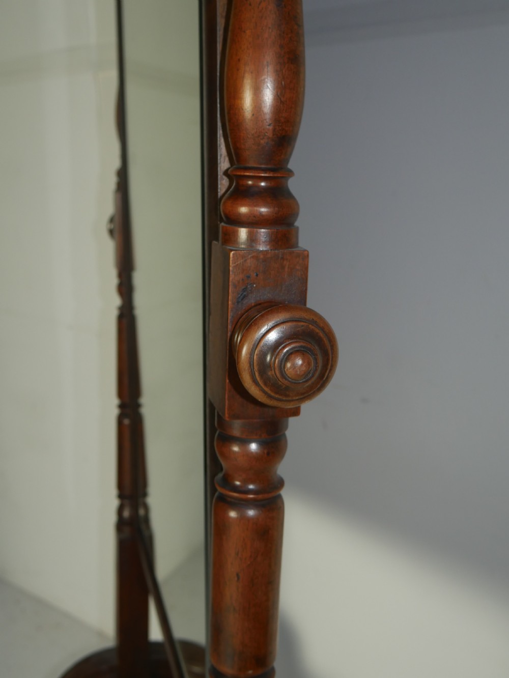 A Regency mahogany cheval mirror featuring turned side supports, finials, adjustable side knobs, and splayed legs on brass castors. View II