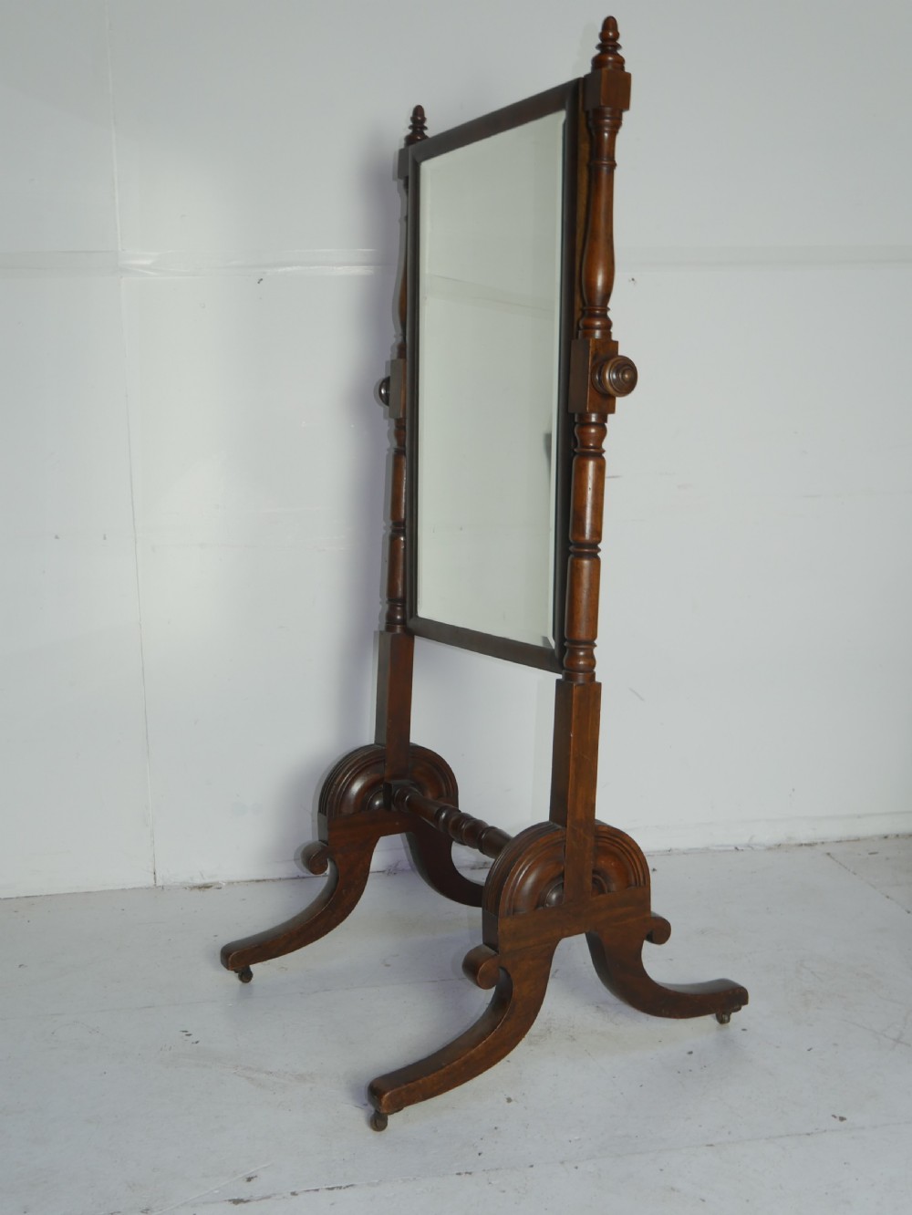 A Regency mahogany cheval mirror featuring turned side supports, finials, adjustable side knobs, and splayed legs on brass castors. View V