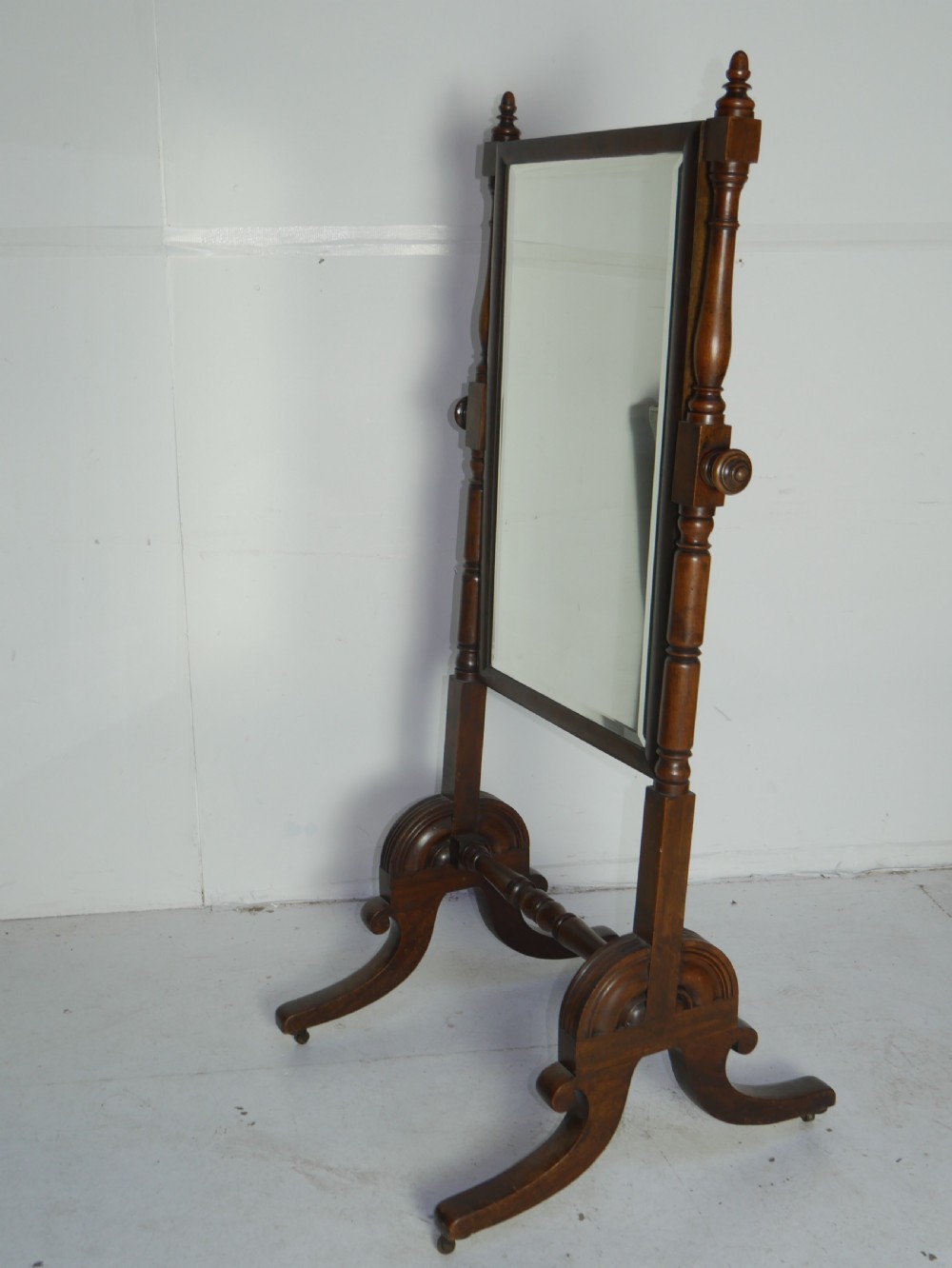 A Regency mahogany cheval mirror featuring turned side supports, finials, adjustable side knobs, and splayed legs on brass castors. View VI