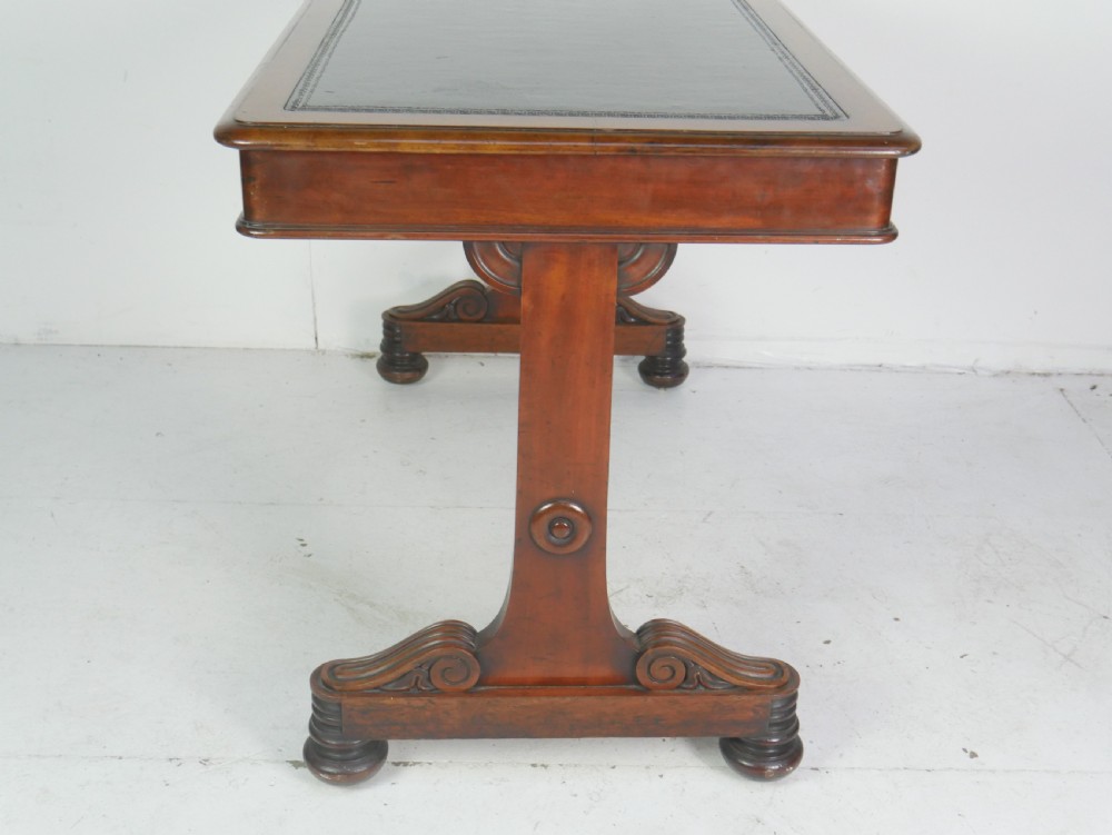 A mahogany writing desk featuring a dark leather inset top, two frieze drawers, and a turned stretcher connecting carved trestle end supports. View III