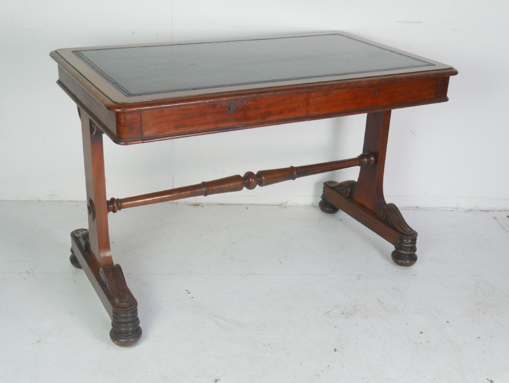 A mahogany writing desk featuring a dark leather inset top, two frieze drawers, and a turned stretcher connecting carved trestle end supports. View XII