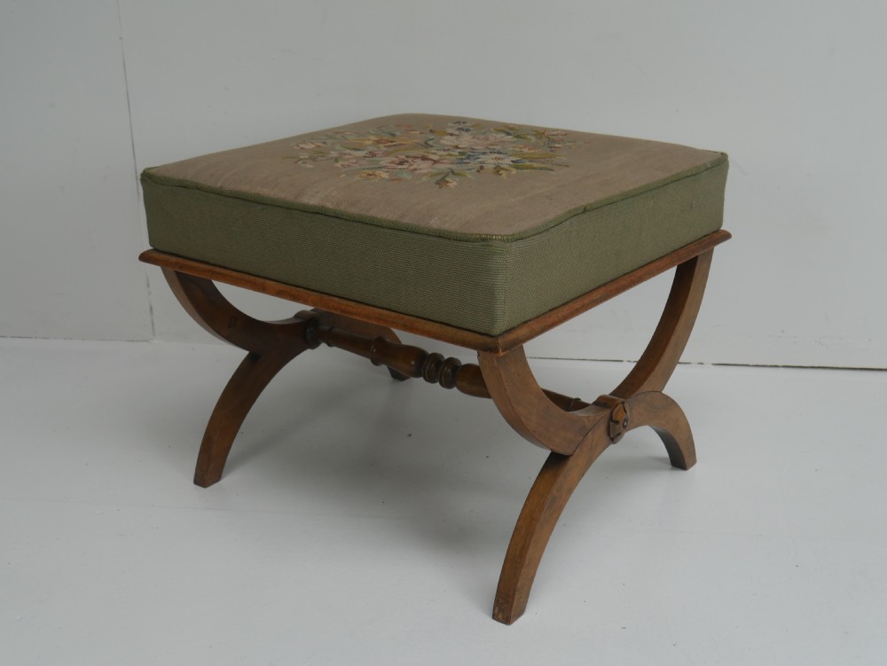 A Regency period rosewood X-frame stool with a turned stretcher bar and a square upholstered top featuring floral needlework set within a green border.