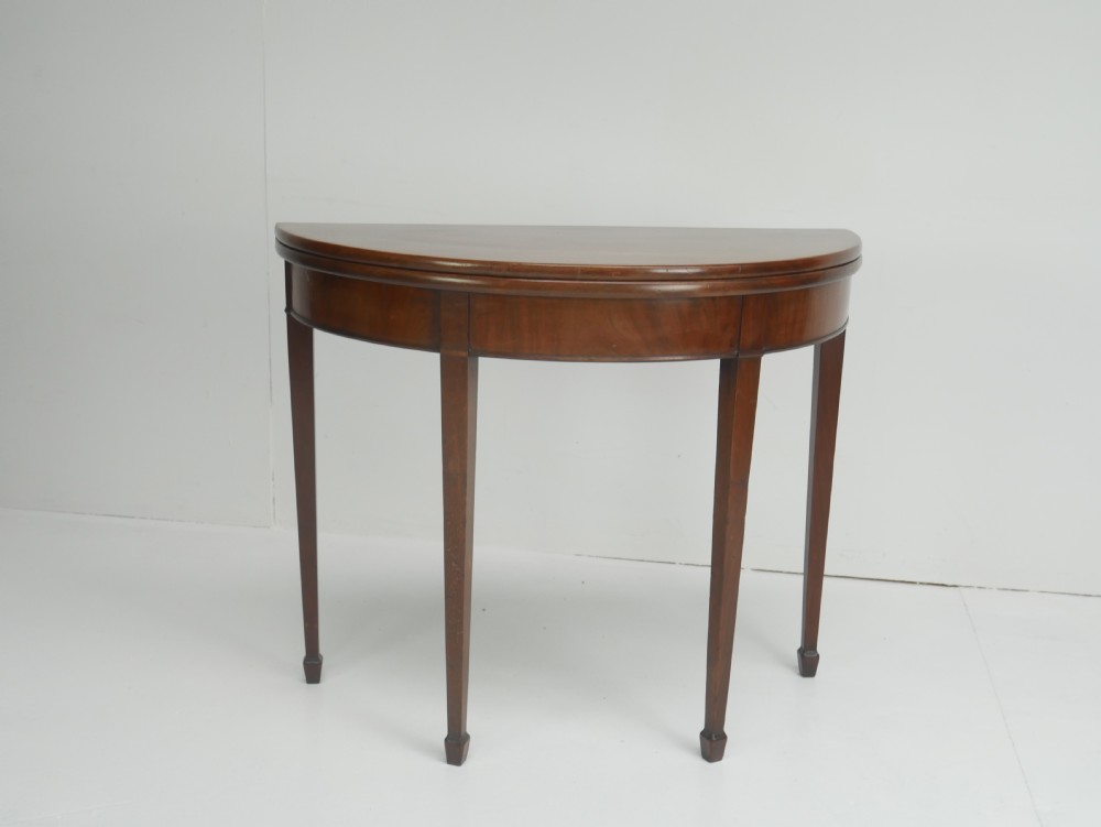 A Georgian mahogany demi-lune side table featuring a semicircular top, a plain apron, and four tapered square legs with spade feet. View XI