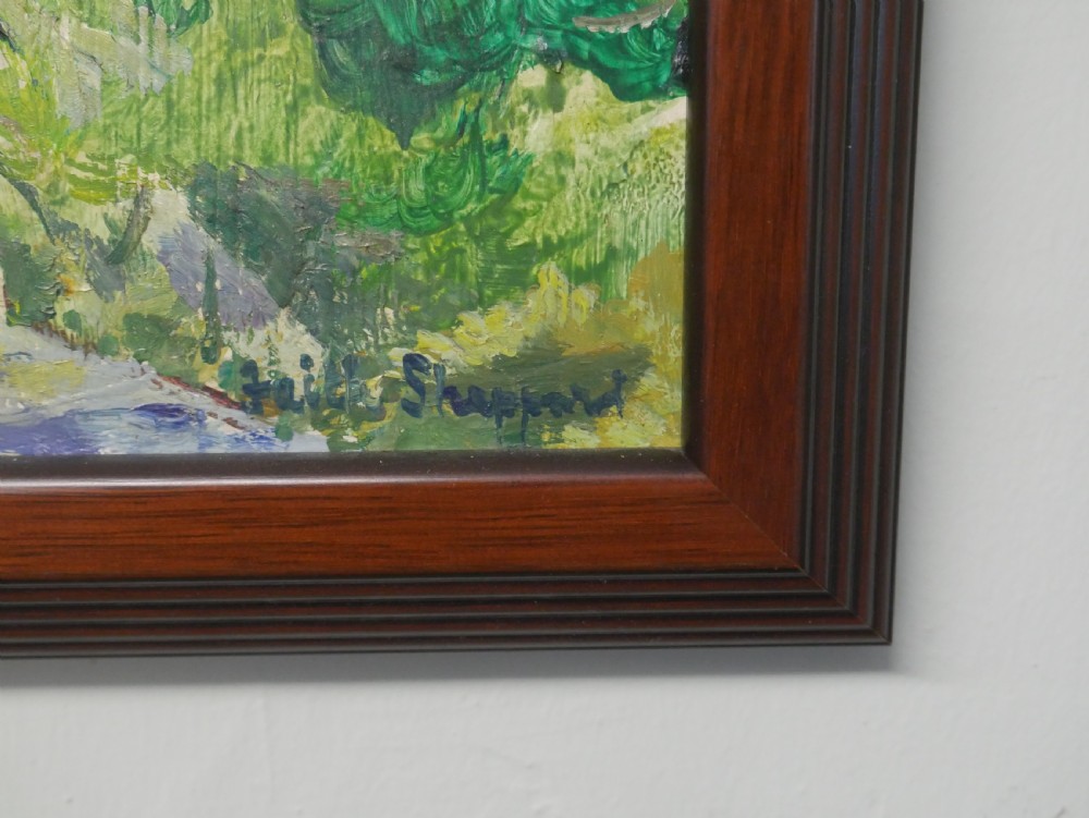 An impressionist oil painting depicting a sunny French village landscape with stone buildings and trees, presented in a dark wooden frame. View III
